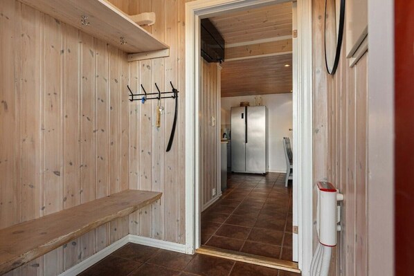 A hallway with wooden walls, a bench, a coat rack, and a refrigerator in the background.