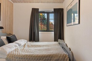 A bedroom with a bed, a window with curtains, a painting on the wall, and a wooden ceiling.