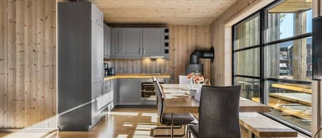 A modern kitchen with wooden cabinets, a dining area with a table and chairs, and large windows offering a view.