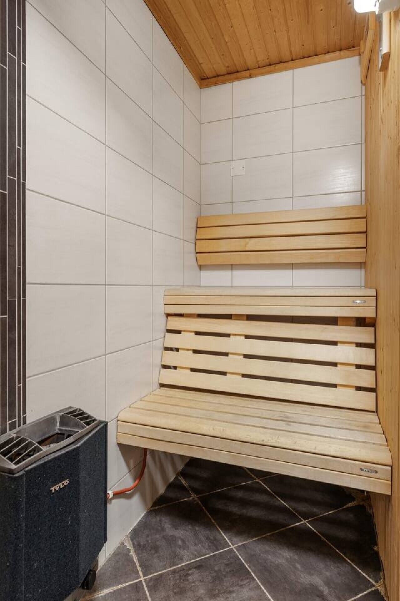 Eine Sauna mit einer Holzbank, gefliesten Wänden und einem Mülleimer.