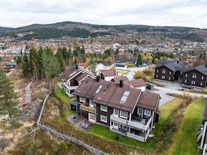 A residential area with multiple houses, a paved driveway, and a view of a town in the distance. - Trysil Ski-in out Apt, Private Sauna, Sleeps 9 (Trysil)
