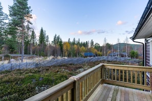 A wooden deck with a view of a forested area and a building in the background. - Trysil Ski-in out Apt, Private Sauna, Sleeps 9 (Trysil)