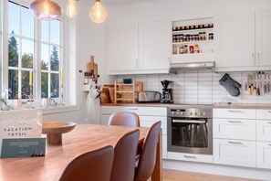 A modern kitchen with white cabinets, a wooden dining table, and a built-in oven. - GO11 Trysil Ski-in out Apt, Private Sauna, Sleeps 9 (Trysil)