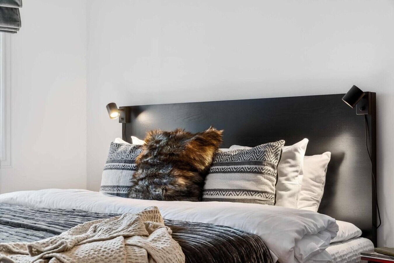 A bed with a black headboard, white pillows, and a blanket.