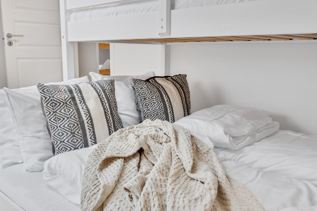 Un lit avec une literie blanche, des coussins à motifs et un plaid tricoté.