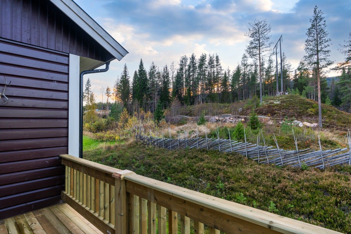 A wooden cabin with a deck overlooking a forested area with a clear sky.