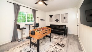 Una habitación con mesa de futbolín, ventilador de techo, sofá y obras de arte en las paredes.