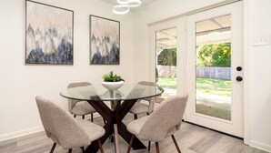 Un comedor con una mesa de vidrio, cuatro sillas y dos cuadros abstractos en la pared.