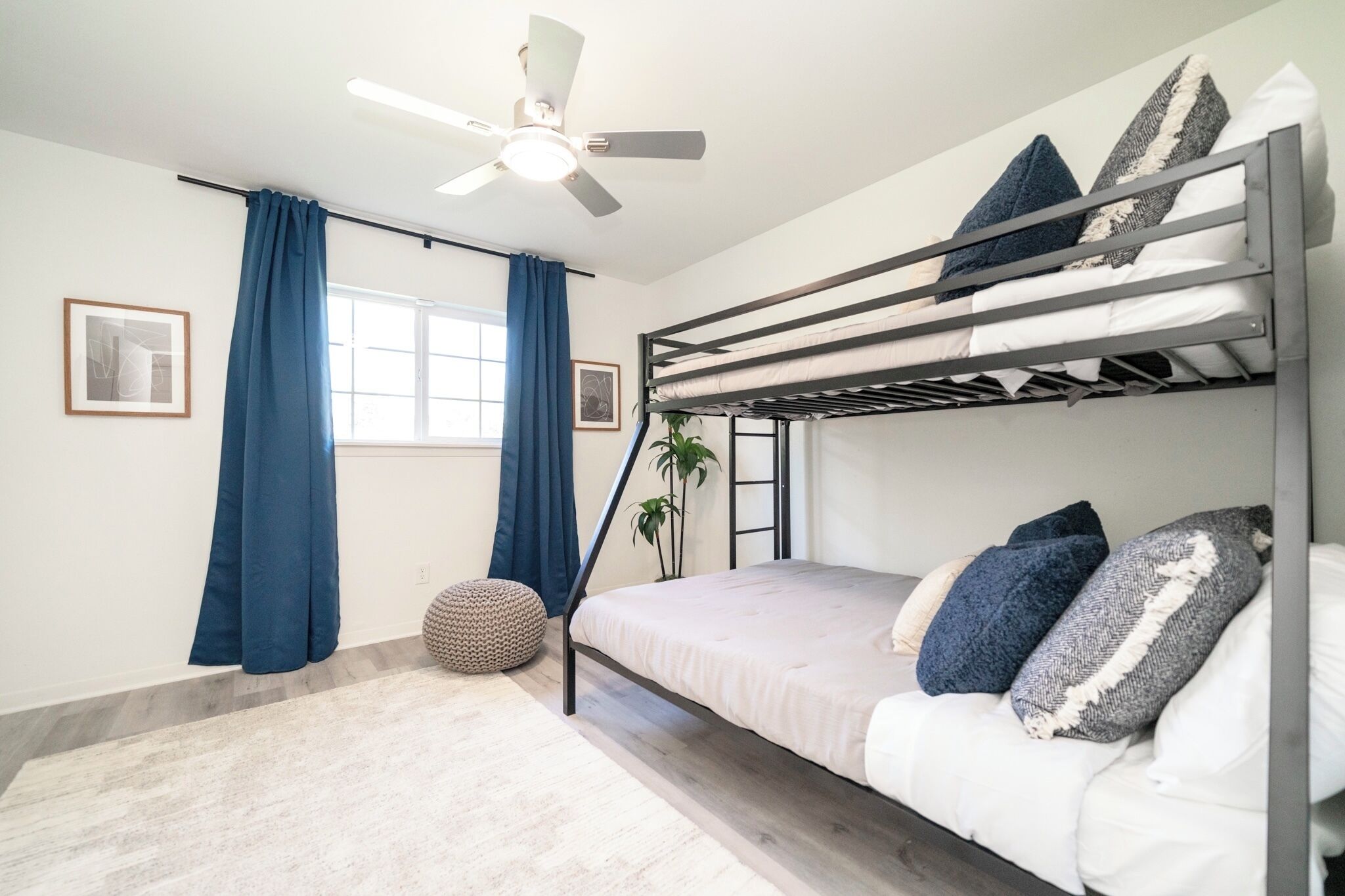 Habitación con literas, ventilador de techo, ventana con cortinas azules y una alfombra redonda pequeña.