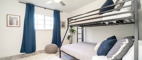 Habitación con literas, ventilador de techo, ventana con cortinas azules y una alfombra redonda pequeña.