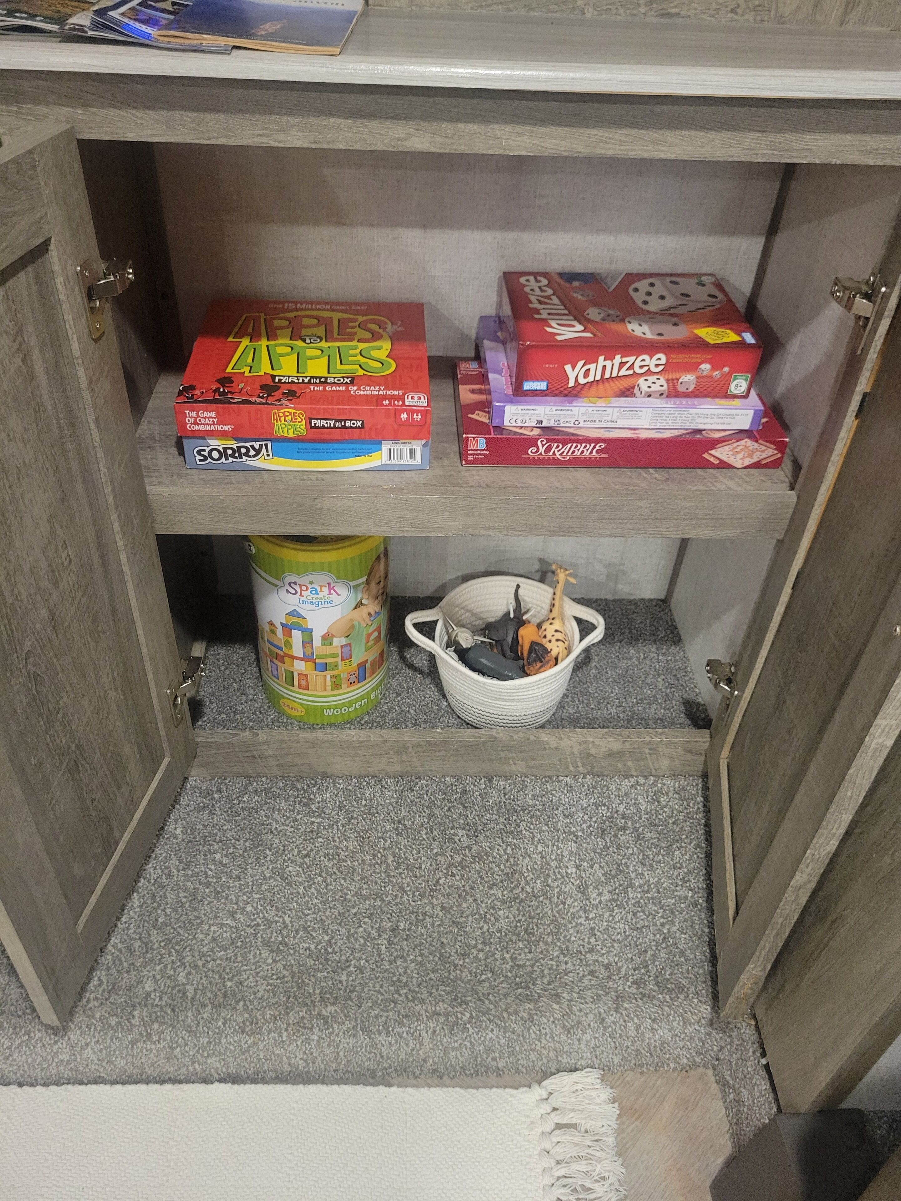 A wooden cabinet with shelves containing board games and a toy storage basket.