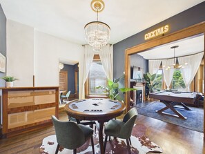 A room with a pool table, a billiards table, a chandelier, and a sign that reads 'COCKTAILS'.