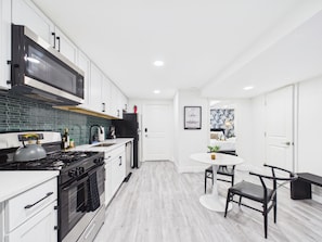 A modern kitchen with white cabinets, a black stove, and a dining area with a round table and two chairs.