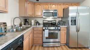 Una cocina moderna con armarios de madera, electrodomésticos de acero inoxidable, incluyendo un microondas, estufa y refrigerador, además de un lavavajillas.