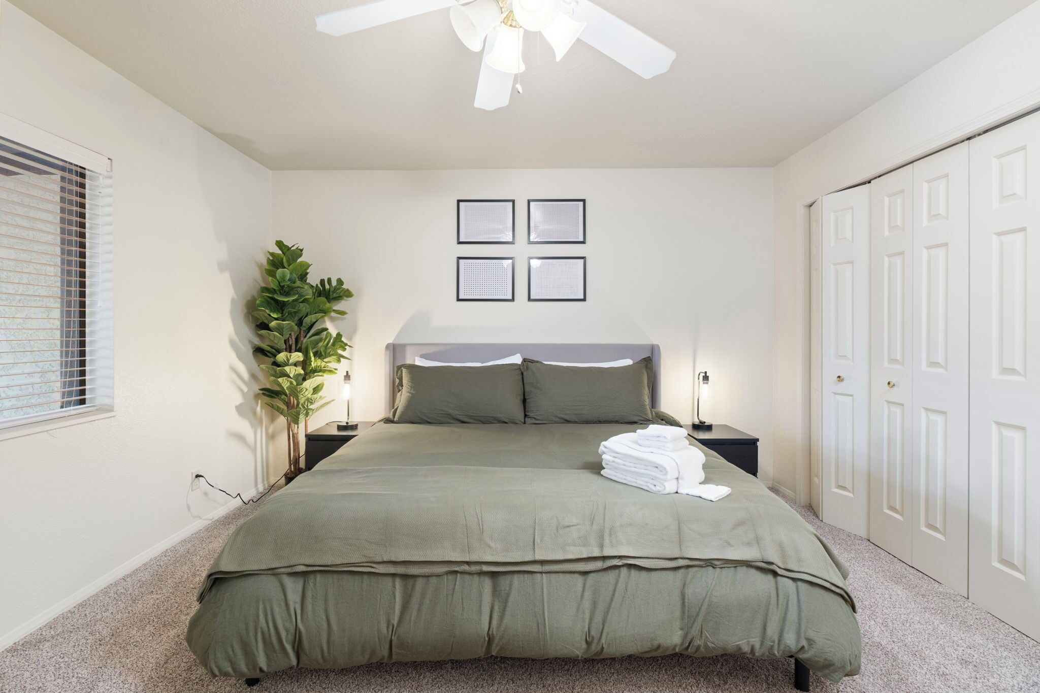 A bedroom with a bed, a ceiling fan, a nightstand, a lamp, a potted plant, and a wardrobe.
