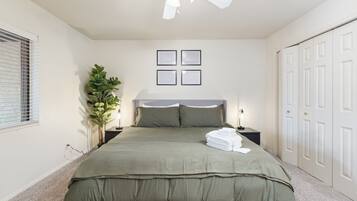 A bedroom with a bed, a ceiling fan, a nightstand, a lamp, a potted plant, and a wardrobe.
