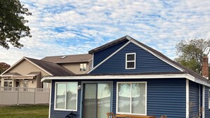 A single-story house with a blue exterior, large sliding glass doors, and a patio with a wooden table and chairs.