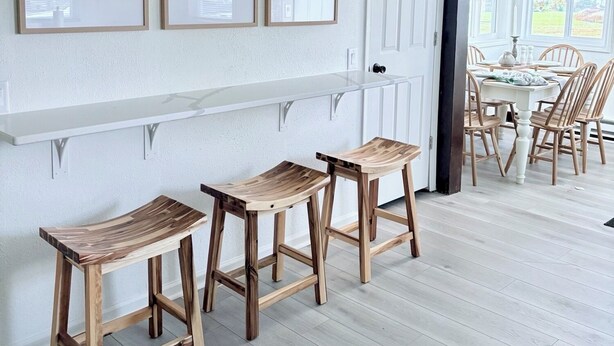 A dining area with a white wall, three framed pictures, and wooden stools.