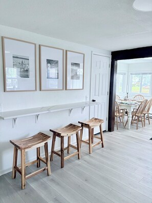 Un coin repas avec un mur blanc, trois tableaux encadrés et des tabourets en bois.