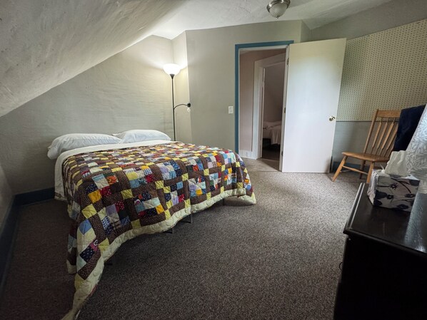 Ein Schlafzimmer mit einem Bett, einer Steppdecke, einer Lampe, einem Sessel und einem Schreibtisch.