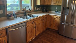 A kitchen with wooden cabinets, stainless steel appliances, a double sink, and a window with a view of the outside. - Back to the Old Farm (Ashland)