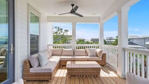 A covered outdoor deck with a wicker sofa, a small table, and a ceiling fan. - Barefoot on 30a by Stay on 30a (Seacrest Beach)