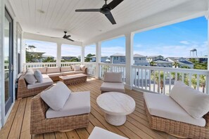 Une terrasse extérieure couverte, aménagée avec des meubles en osier, une table ronde et des ventilateurs de plafond.