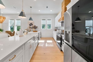 Una cocina moderna con armarios blancos, suelo de madera e iluminación colgante.
