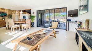Un salon moderne avec une table à manger en bois, des chaises en osier, un canapé et une grande porte-fenêtre coulissante donnant sur une terrasse extérieure.