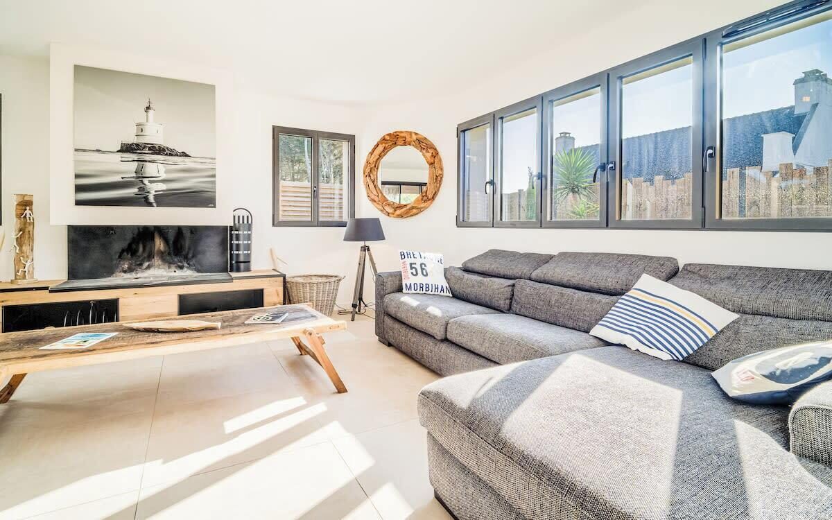A modern living room with a fireplace, grey sofa, and large windows.