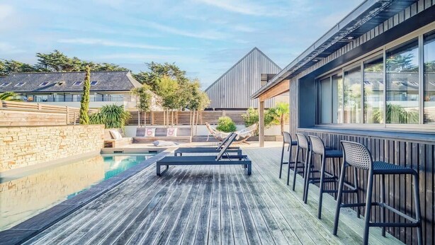 Une terrasse en bois avec une piscine, des chaises longues et un espace bar.