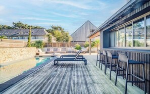 Une terrasse en bois avec une piscine, des chaises longues et un espace bar.