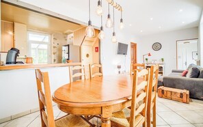 A modern kitchen with a wooden dining table and chairs, a built-in oven, and hanging light fixtures.