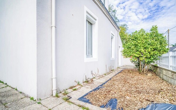 A white building with a small tree in the yard, a blue tarp on the ground, and a white fence.