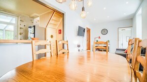 Ett modernt kök med en bänkskiva i trä, ett runt matbord och trästolar. En tv är monterad på väggen och ovanför den hänger en klocka.