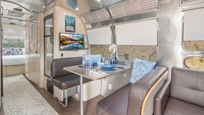 Een modern interieur van een camper, met een eethoek, zitplaatsen en een tv.