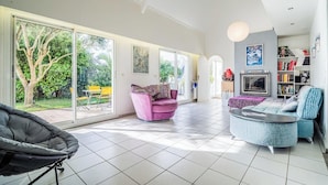 Un salon spacieux avec de grandes fenêtres, un fauteuil violet, un canapé bleu et un téléviseur fixé au mur.