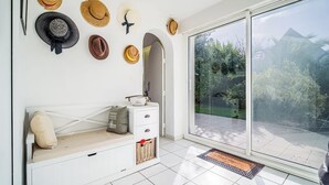 Une pièce avec un banc blanc, une petite armoire blanche et une porte vitrée donnant sur un balcon avec vue sur la verdure.