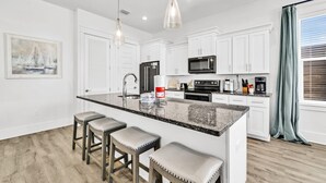 A modern kitchen with white cabinets, a granite countertop, and a central island with bar stools. - Destin/Miramar 4BR/4BA | Golf Cart | Pool | 1st Floor BR | Pets OK | Fenced Yard (Miramar Beach)