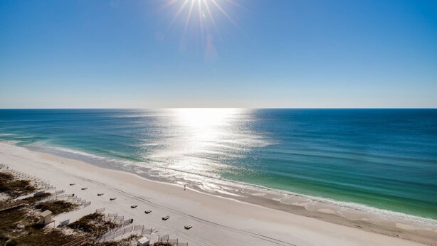 A beach with a clear sky, a bright sun, and calm ocean waters. - Destin/Miramar 4BR/4BA | Golf Cart | Pool | 1st Floor BR | Pets OK | Fenced Yard (Miramar Beach)