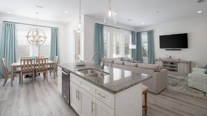 A modern kitchen with a central island, white cabinetry, and a dining area with a wooden table and chairs. - Destin/Miramar 4BR/4BA | Golf Cart | Pool | 1st Floor BR | Pets OK | Fenced Yard (Miramar Beach)