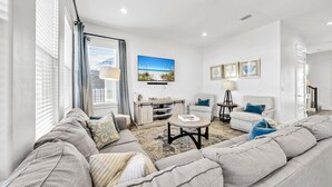 A modern living room with a grey sofa, a coffee table, and a TV mounted on the wall. - Destin/Miramar 4BR/4BA | Golf Cart | Pool | 1st Floor BR | Pets OK | Fenced Yard (Miramar Beach)