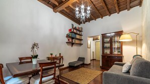 A living room with a wooden dining table, chairs, a sofa, a chandelier, a bookshelf, and a cabinet. - One Bedroom Apartment (ROMA)