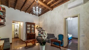 A spacious living room with a wooden dining table, a chandelier, a sofa, and a bookshelf. - One Bedroom Apartment (ROMA)
