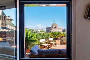 Vista dalla finestra su un cortile con un edificio in pietra, arredi da esterno e piante.