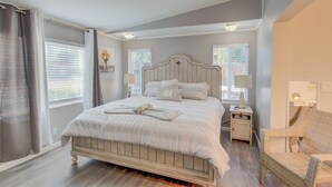 Um quarto com cama, mesas de cabeceira, uma cadeira e uma janela com cortinas.