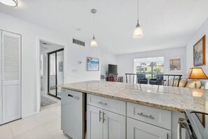 A modern kitchen with granite countertops, white cabinetry, and pendant lighting. - OV 222 Tennis Court View - Welcome To Paradise! (Fort Pierce)