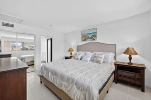 Un dormitorio con una cama grande, dos mesitas de noche con lámparas, un cuadro en la pared y vistas a través de una puerta.