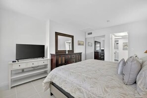 A bedroom with a bed, a TV, a dresser, and a mirror. - OV 222 Tennis Court View - Welcome To Paradise! (Fort Pierce)