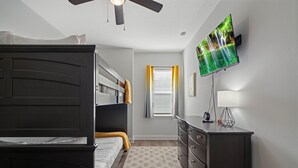 Une chambre avec un lit superposé, une commode, un téléviseur et une fenêtre avec des rideaux.